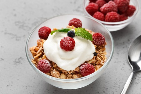 Granola with greek yogurt and raspberries in bowls on grey background,の写真素材