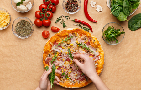 Woman adding rocket salad to pizza, decorating it with various ingrediends, top viewの写真素材
