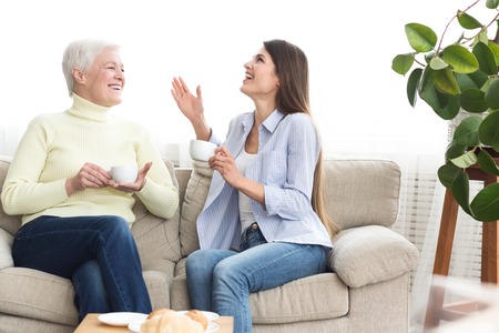 Mother and daughter drinking coffee and talking on couch at home