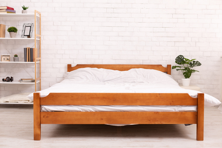 Bedroom interior. Empty wooden framed double bed with two pillows and white blanket, free space. Real photo.の写真素材
