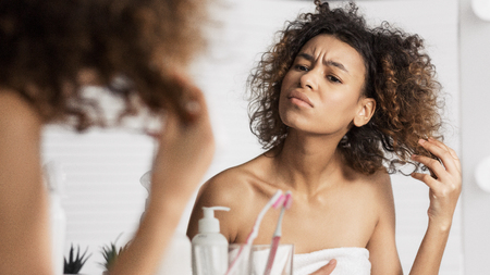 Afro-american girl frowning and looking intently on her face in mirror. Dried hair detected concept