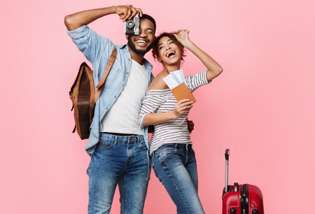 Ready for vacation. Happy couple with suitcase and tickets over pink backgroundの写真素材
