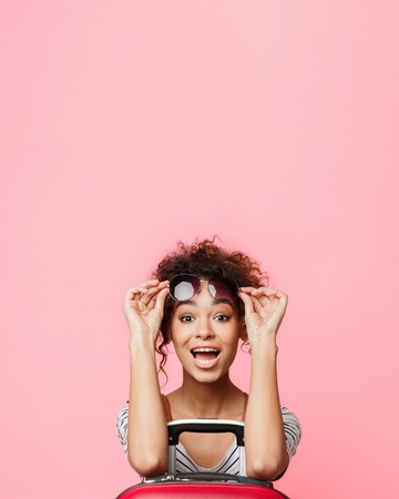 Dream trip. Surprised woman in sunglasses looking at camera over pink background, copy spaceの写真素材