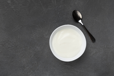 Bowl of yogurt and spoon on darck background, top view, copy spaceの写真素材