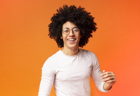 Carefree joyful handsome african-american man with bushy hairstyle smiling at camera on orange backgroundの写真素材