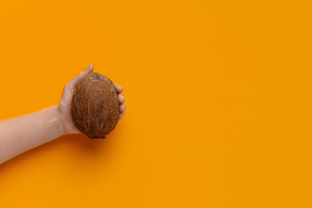 Female hand holding coconut on yellow background, top view, copy space. What about coconut conceptの写真素材