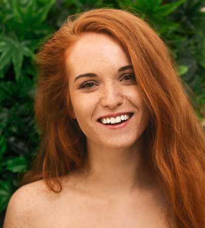 Sunny redhead girl with freckles smiling at camera, closeup portraitの写真素材