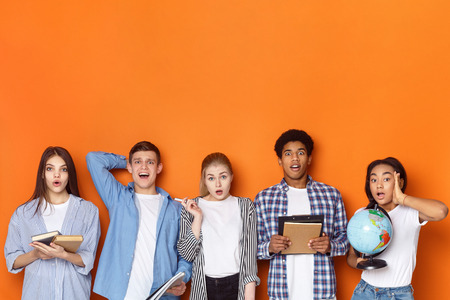 Education concept. Surprised students looking at camera over orange background with free spaceの写真素材