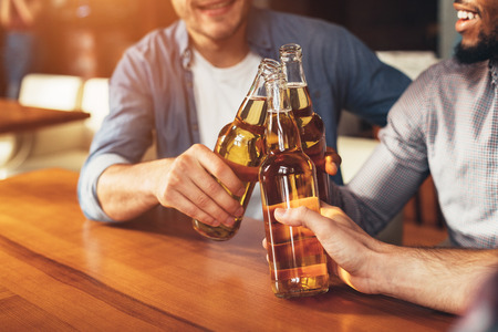 Friends clinking bottles of beer, resting together in barの写真素材