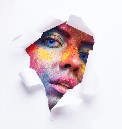 Fashion minimalistic portrait. Woman face with artistic bright makeup in white paper holeの写真素材