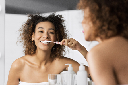 Smiling young afro-americam woman with toothbrush cleaning teeth at bathroom. Teeth whitening conceptの写真素材