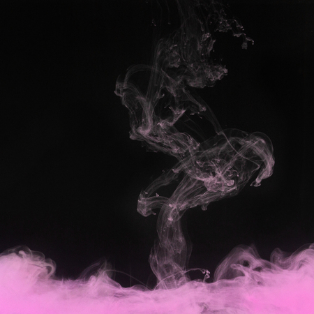 Pink smoke swirling underwater on black background.の写真素材