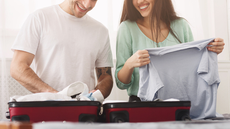 Couple packing clothes into suitcase, preparing for honeymoon vacation at homeの写真素材