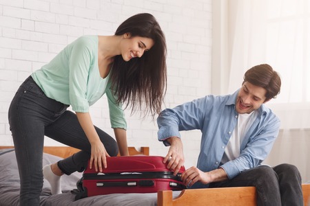 Couple closing full suitcase, preparing for vacation at homeの写真素材