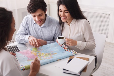 Newlyweds choosing trip on honeymoon, looking at map in travel agency