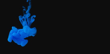 Cloud of blue ink underwater on black background, copy space.