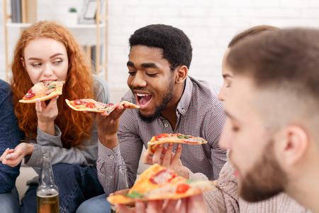 Pizza time. Friends eating and drinking beer, spending time together at homeの写真素材