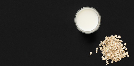 Glass of milk and pile of oat flakes on black background, top view, copy space. Lactose free milk conceptの写真素材