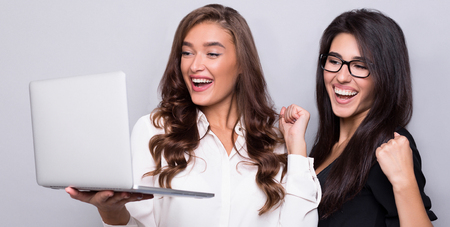 Yes, we did it. Happy business women looking at laptop and smiling, gray studio background, panorama