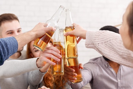 Celebrate meeting. Friends clinking beer bottles, having fun at homeの写真素材