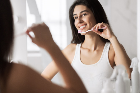 Smiling young woman with toothbrush cleaning teeth at bathroom. Morning dental hygiene conceptの写真素材