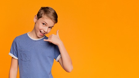 Call me, baby. Cute boy put his hand to his ear and smiling, orange panorama background with empty...
