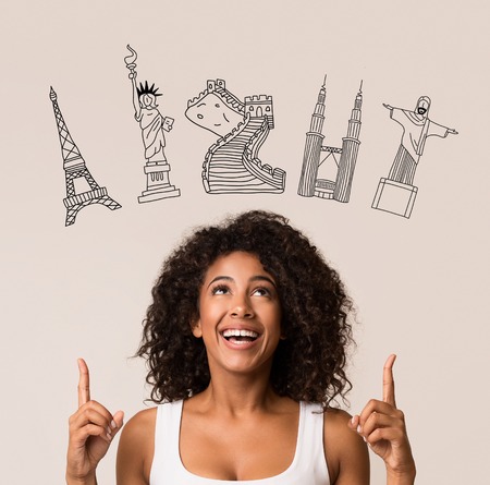 Happy afro-american woman pointing fingers at tourist attractions drawn on grey background. Choose your trip conceptの写真素材