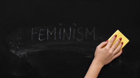 Fight for female rights. Woman cleaning word FEMINISM on chalkboard, panorama