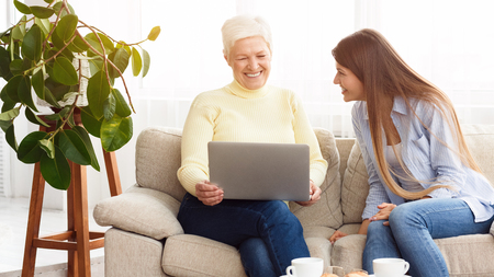 Daughter showing mother funny videos on laptop, having rest at home