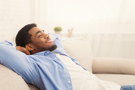 Lazy millennial african american man relaxing at home, holding hands behind head, empty spaceの写真素材