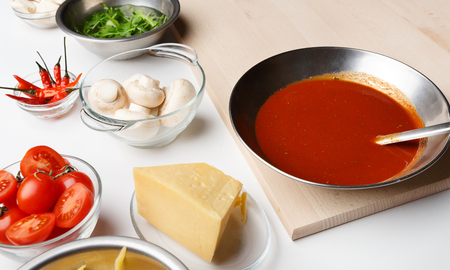 Pizza cooking ingredients. Cheese, mushrooms and sauce in bowls on kitchen table