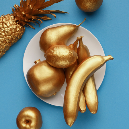 Golden fruits on plate on blue background. Shiny fruits conceptの写真素材