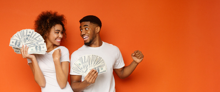 Happy young black couple holding lots of dollar currency and smiling to each other, panorama with free spaceの写真素材