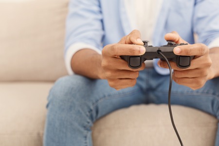 Unrecognizable african american guy playing video games at home, holding joystick in hands, free...