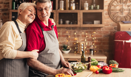 Thanks for dinner. Grateful senior woman hugging her husband that preparing healthy lunch at kitchen, panorama with empty spaceの写真素材