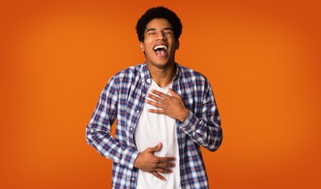 Cant stop laughing. Guy touching stomach, hearing jokes over orange backgroundの写真素材