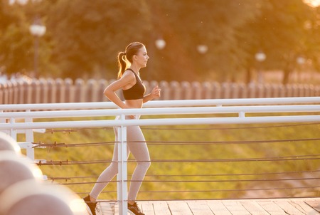 Beautiful sporty young woman running over bridge early in morning, sunflare effect, empty space