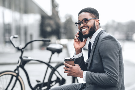 No time for break. Millennial businessman talking on phone during his lunch outdoors with bicycle nearbyの写真素材
