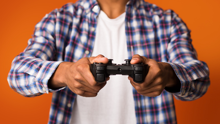 African-american guy playing video games online, holding joystick over orange background, closeup
