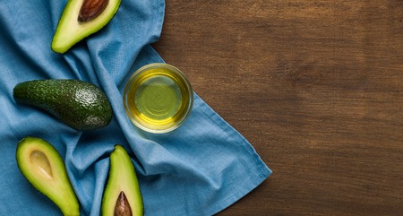 Sliced and whole avocadoes and oil in bowl on blue napkin over wooden background top view, copy space.の写真素材