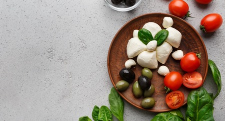 Buffalo mozzarella , olives, fresh herbs and tomatoes on plate at grey background, top view.の写真素材