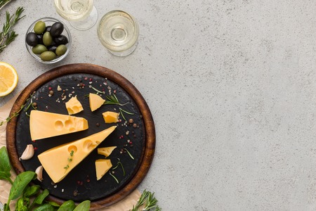 Cheese on board, two glasses of wine, olives, fresh herbs and spicies over concrete background, top view, copy spaceの写真素材