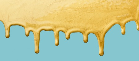 Golden paint dripping on blue background, copy spaceの写真素材