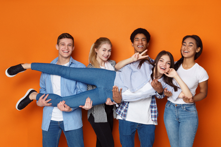 Teenagers holding friend and having fun over orange studio backgroundの写真素材