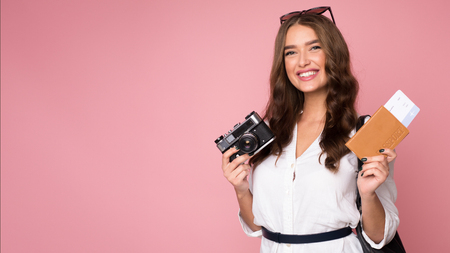 Happy traveller with retro camera and tickets looking at camera over pink background, copy spaceの写真素材