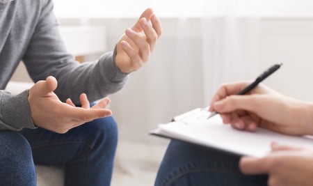 Psychotherapist writing notes, assessing patients health and giving diagnosis to man sitting on couch during counseling session , panorama, free spaceの写真素材