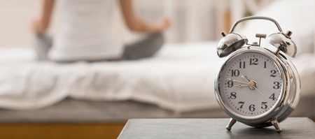 Healthy lifestyle contemplation. Woman meditating with alarm clock on foreground, panorama