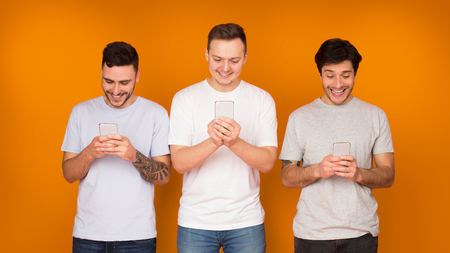 Internet addiction. Men with smartphones, using social networks over orange backgroundの写真素材