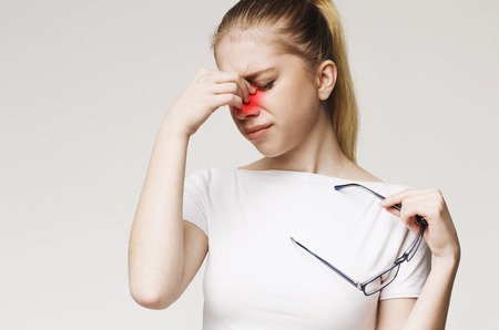 Tired woman suffering from eye pain, holding glasses and massaging her nose
