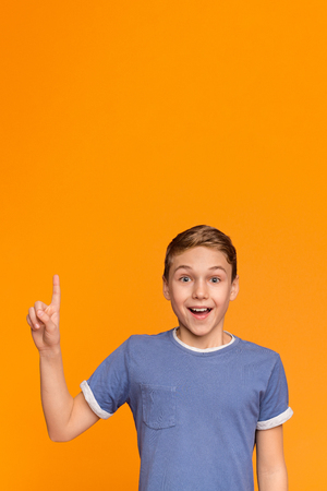 Eureka! Excited teenage boy have great idea, pointing finger up with opened mouth, orange background with free spaceの写真素材